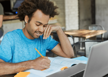 Jovem estudando com laptop em cafeteria moderna.