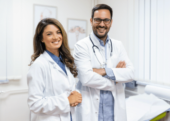 Médica e médico sorrindo em consultório iluminado.