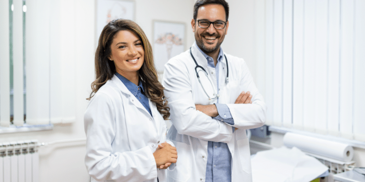Médica e médico sorrindo em consultório iluminado.