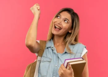 Jovem feliz segurando livros e com mochila nas costas.