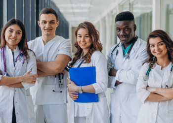 Jovens profissionais de saúde em uniforme posam em hospital.