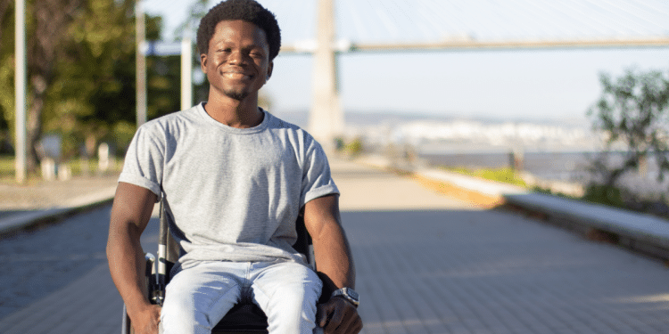 Jovem em cadeira de rodas sorri ao ar livre em dia ensolarado.