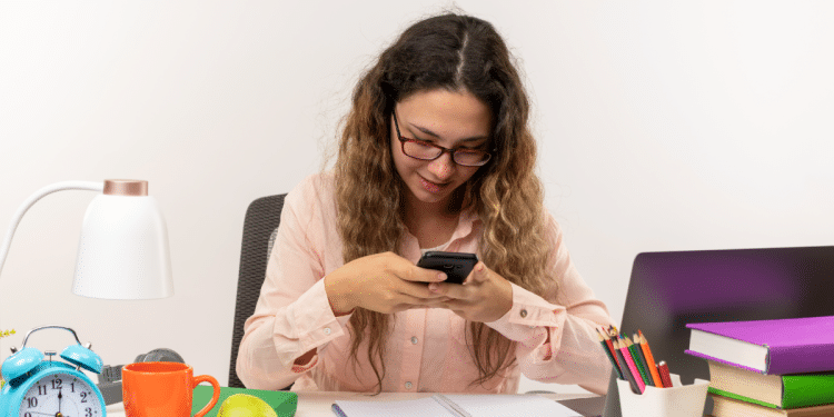 Jovem estudante distraída com celular em dia de estudos.