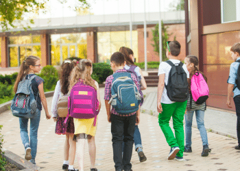 Grupo de crianças caminhando para escola em área externa.