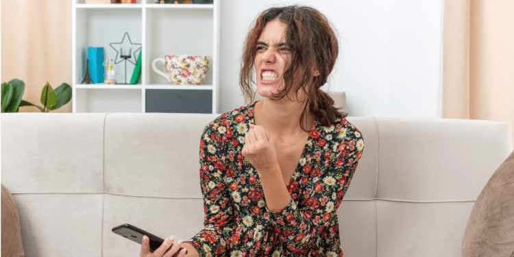 Jovem irritada reage ao celular em momento de frustração caseira.