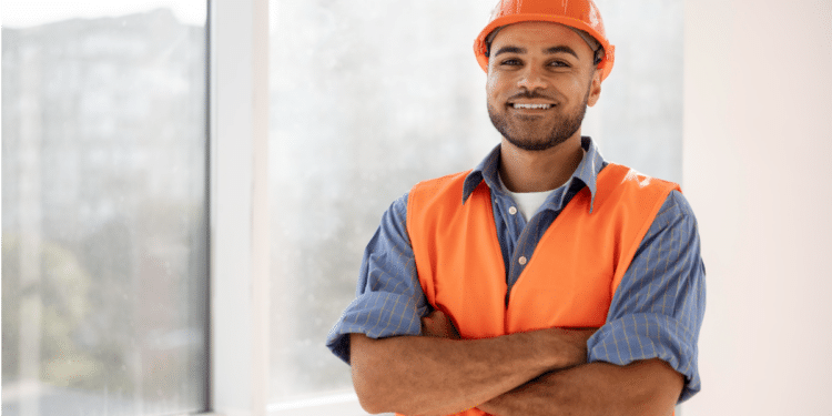Técnico em segurança do trabalho sorridente com uniforme e capacete laranja.
