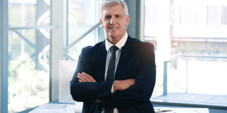 Homem de terno e com os braços cruzados no seu ambiente de trabalho.
