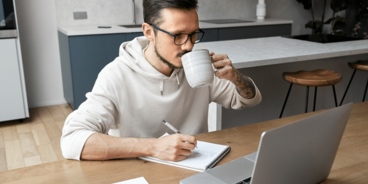 Homem trabalhando em casa enquanto toma café durante videoconferência.