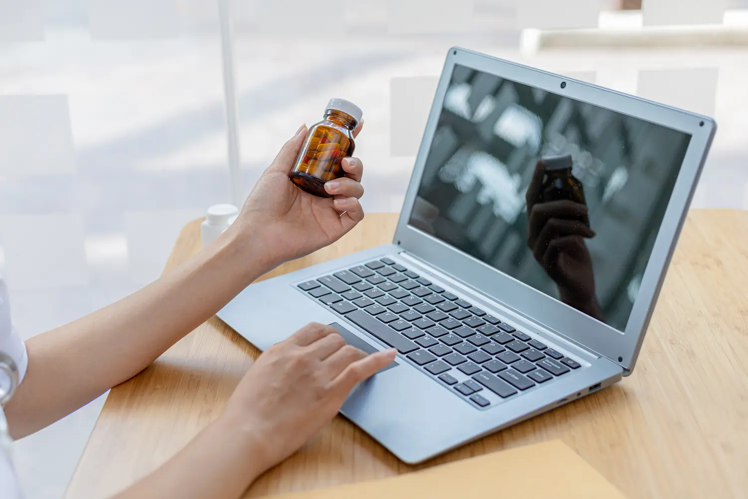 Pessoa segura frasco de medicamento diante de um notebook durante uma compra pela internet.