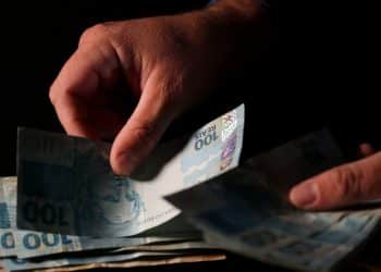 Mãos contam cédulas de R$ 100, imagem que ilustra a matéria sobre a antecipação do pagamento do Abono Salarial PIS/Pasep em julho de 2026