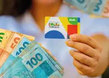 Beneficiária segura cartão do Bolsa Família e notas de real durante o calendário de pagamentos de julho.