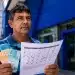 Beneficiário brasileiro segurando cédulas de real e calendário de pagamentos do INSS em frente a uma agência com fachada azul.