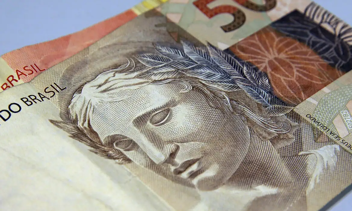 Detalhe de cédula de 50 reais, referência ao cálculo do Abono Salarial PIS/Pasep 2026, que divide o salário mínimo de R$ 1.621 em doze parcelas.