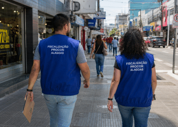 Dois fiscais do Procon de Alagoas caminham por uma rua comercial durante atividade de fiscalização.