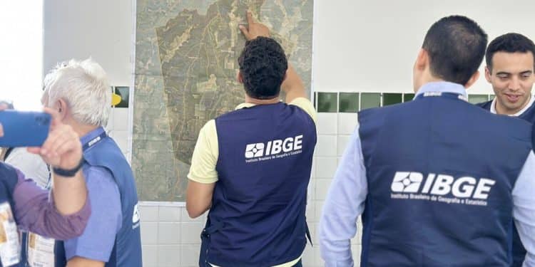 Servidores com colete do IBGE analisam mapa de município fixado na parede durante trabalho de campo