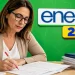 Professora corrigindo redação do Enem 2026 em mesa de trabalho, com materiais de avaliação e slogan ao fundo.