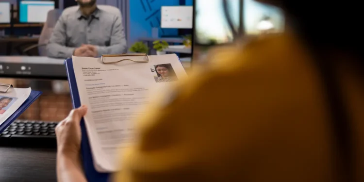 Recrutadora analisa currículo com foto durante entrevista de emprego por videochamada.