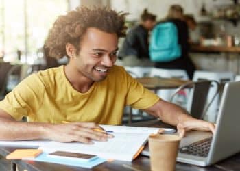 Estudante sorridente estuda em notebook com caderno e anotações, situação que remete aos cursos livres usados como horas complementares na faculdade