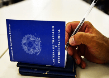 Mão masculina assina carteira de trabalho azul com caneta, documento do Ministério do Trabalho, simbolizando a regra da CLT que define quando o período de férias pode começar.
