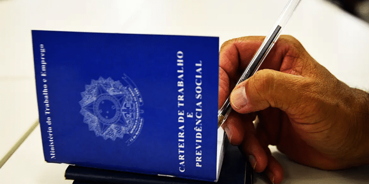 Mão masculina assina carteira de trabalho azul com caneta, documento do Ministério do Trabalho, simbolizando a regra da CLT que define quando o período de férias pode começar.