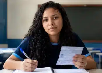 Estudante brasileiro em sala de aula segurando cartão de inscrição e caneta, em preparação para o Enem