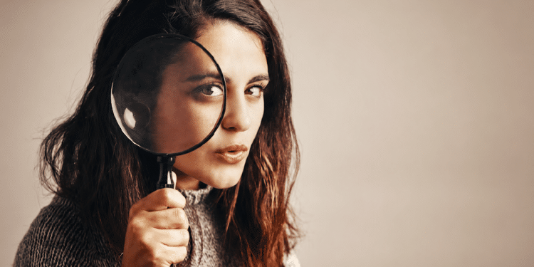 Mulher jovem segura lupa em frente ao olho realçando olhar atento e cabelo castanho solto, simbolizando a dúvida entre escanear ou scanear.