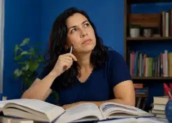 Mulher consulta livros abertos enquanto reflete sobre a grafia correta de autossabotagem.