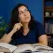 Mulher consulta livros abertos enquanto reflete sobre a grafia correta de autossabotagem.