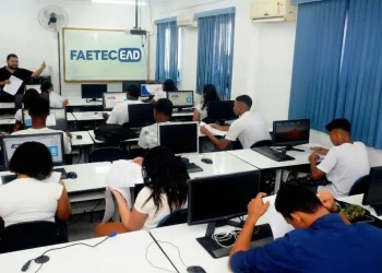 Sala de aula de informática com alunos em computadores durante curso EAD da Faetec, destacando inscrições abertas para vagas gratuitas.