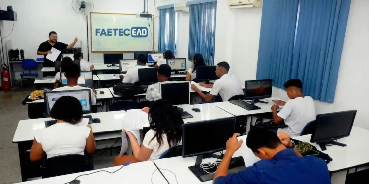 Sala de aula de informática com alunos em computadores durante curso EAD da Faetec, destacando inscrições abertas para vagas gratuitas.