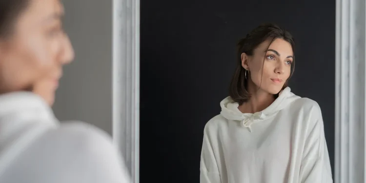 Mulher observando o próprio reflexo no espelho, representando a reflexão pessoal e o hábito de falar sozinho.
