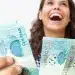 Mulher segurando cédulas de dinheiro representando liberação de pagamento de benefício de R$ 2.621 em julho