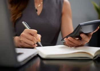 Mulher calcula renda com calculadora e anotações em mesa de trabalho, simbolizando o limite de renda para o Prouni 2026.