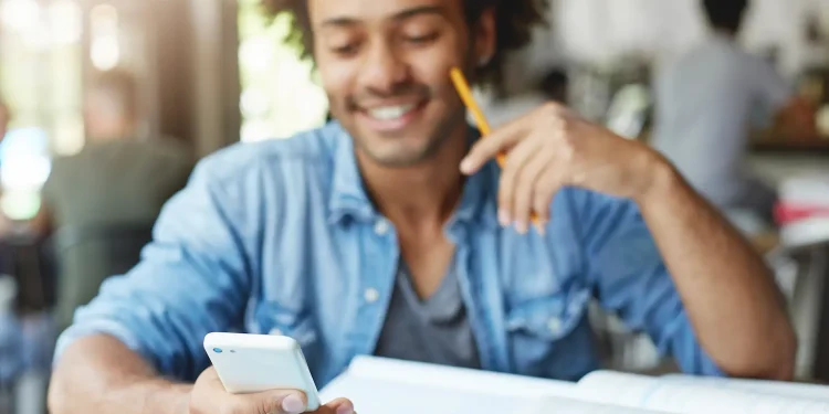 Estudante consulta simulados e exercícios do Enem pelo celular enquanto estuda.