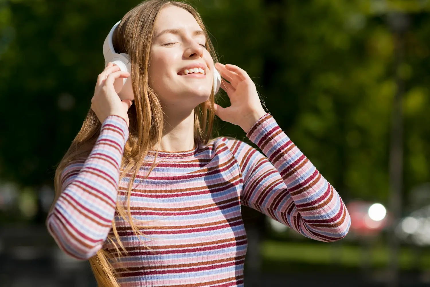 Mulher sorridente escuta música com fones de ouvido em uma área ao ar livre.