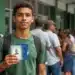Jovem segura documentos de identificação com uma fila de pessoas ao fundo, representando o mutirão para emissão da Carteira de Identidade Nacional (CIN), o novo RG.