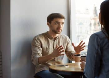 Homem gesticula enquanto fala com uma mulher em uma mesa de café, ilustrando o comportamento de quem fala em excesso
