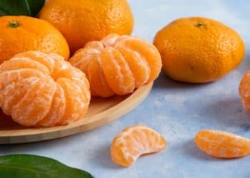 Tangerinas inteiras e descascadas sobre bandeja de madeira, fruta cujo nome gera dúvida entre as grafias ponkan e poncã.