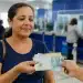 Beneficiária recebe dinheiro em agência bancária, representando o pagamento de atrasados previdenciários.