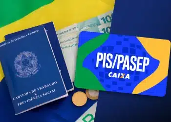 Carteira de trabalho, notas de 100 reais, moedas e cartão PIS/PASEP Caixa sobre bandeira do Brasil, simbolizando o pagamento de R$ 4.421 do PIS/Pasep.
