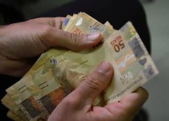 Mãos contam cédulas de 50 reais, referência ao Abono Salarial PIS/Pasep de até R$ 1.621 pago conforme o tempo trabalhado em 2024.