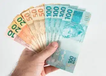 Mão segurando cédulas de real representando o pagamento de salários no quinto dia útil de julho