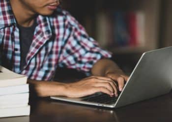 Imagem ilustrativa de estudante estudando com notebook e pilhas de livros, representando o Academia Enem 2026, cursinho gratuito da Prefeitura de Fortaleza com 8 mil vagas para o exame.