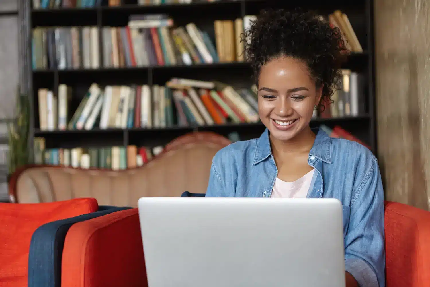 Jovem sorrindo enquanto utiliza notebook em ambiente de estudo, representando processo seletivo da Faetec para cursos EAD.