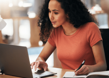 Mulher utiliza notebook e faz anotações durante consulta a vagas para Psicólogo e Assistente Social.