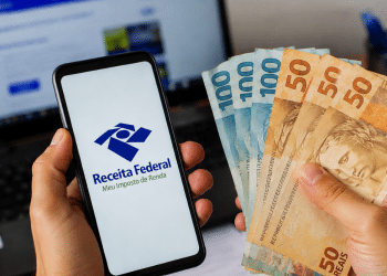 Celular com acesso à Receita Federal ao lado de notas de dinheiro representando dados de renda média dos trabalhadores brasileiros.
