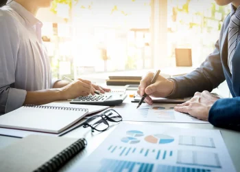 Profissionais analisam gráficos e dados financeiros em uma mesa de trabalho com calculadora e documentos.