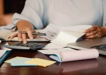 Profissional confere holerites e documentos com calculadora e notebook sobre a mesa, simbolizando a conferência do valor pago quando há proposta de redução salarial.