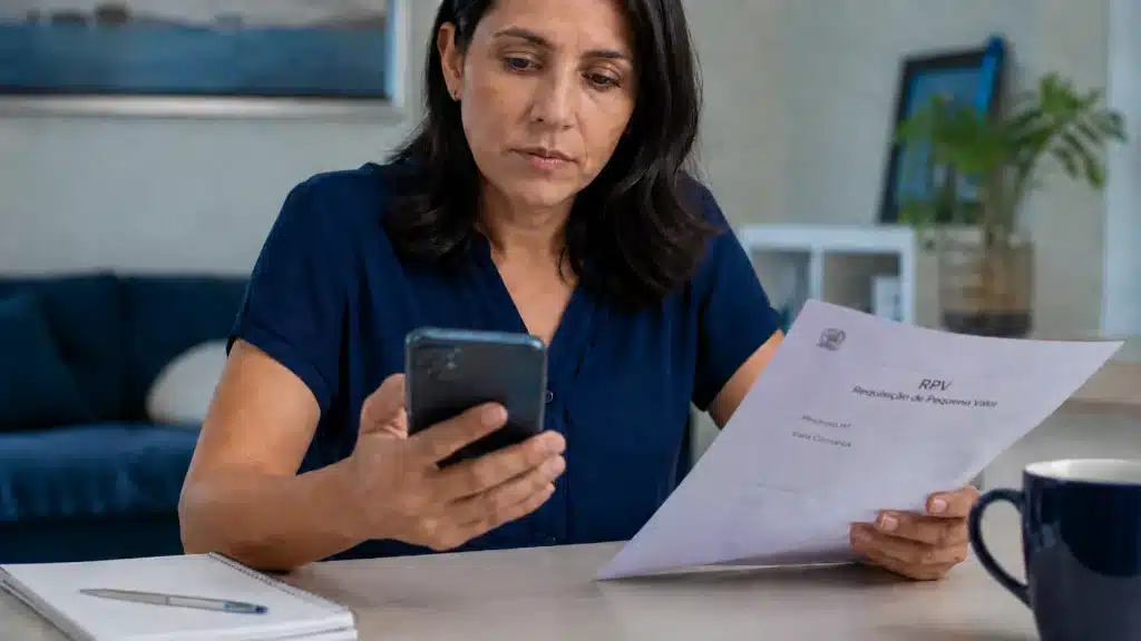 Beneficiária consulta informações de RPV em documento e celular, representando o processo de resgate simples de valor previdenciário.