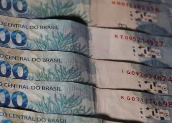 Notas de 100 reais enfileiradas, ilustrando os valores do abono salarial, do lote extra e do ressarcimento das cotas do PIS/PASEP.